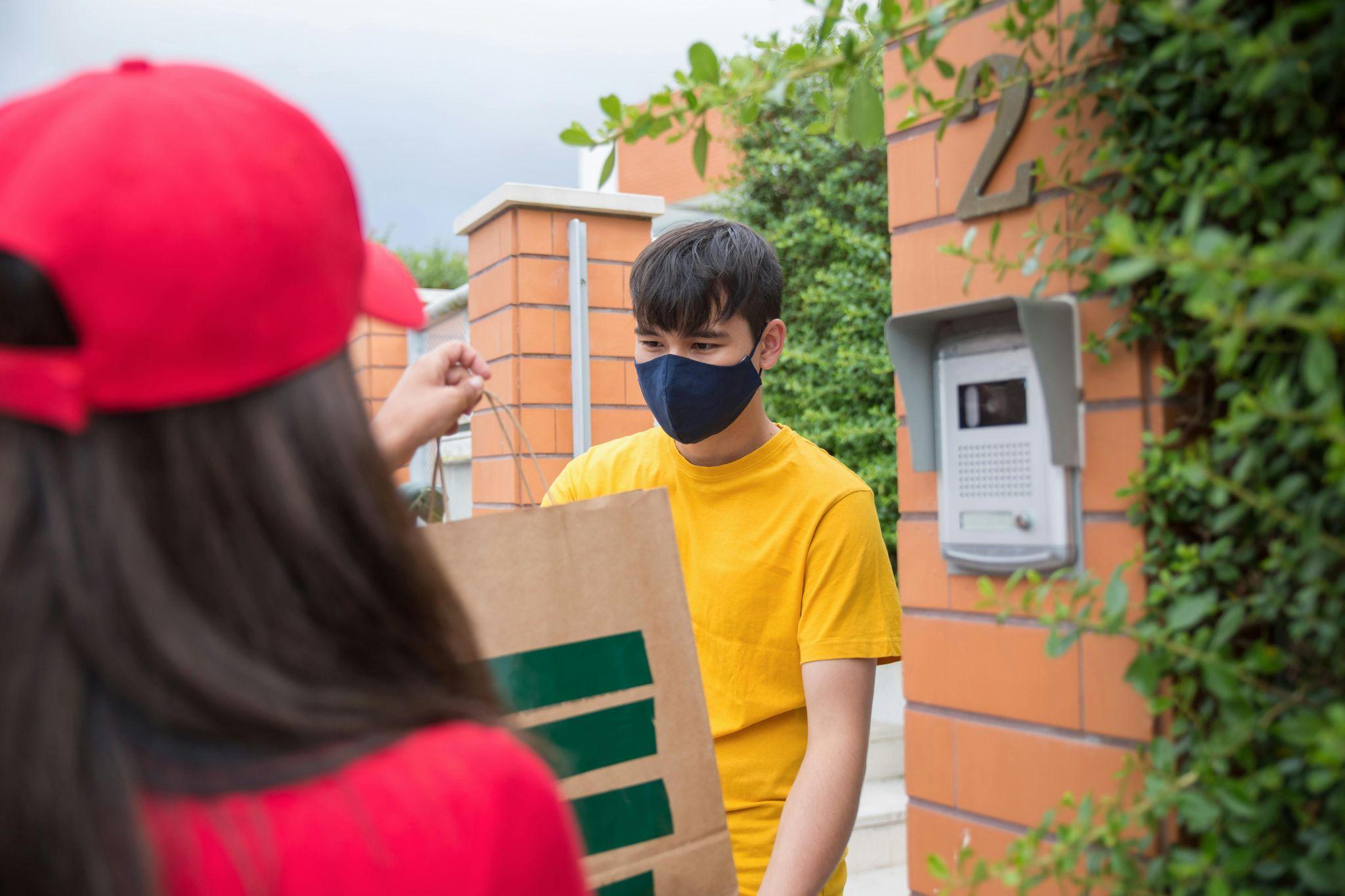 A woman receiving a delivery from a delivery man with an intercom system in the background.